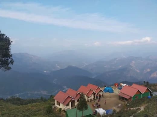 hilltop camp with red-roofed cottages above layered blue mountains